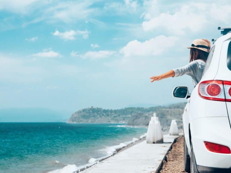 a woman with her arm stretched out the window of her SUV driving along the coast