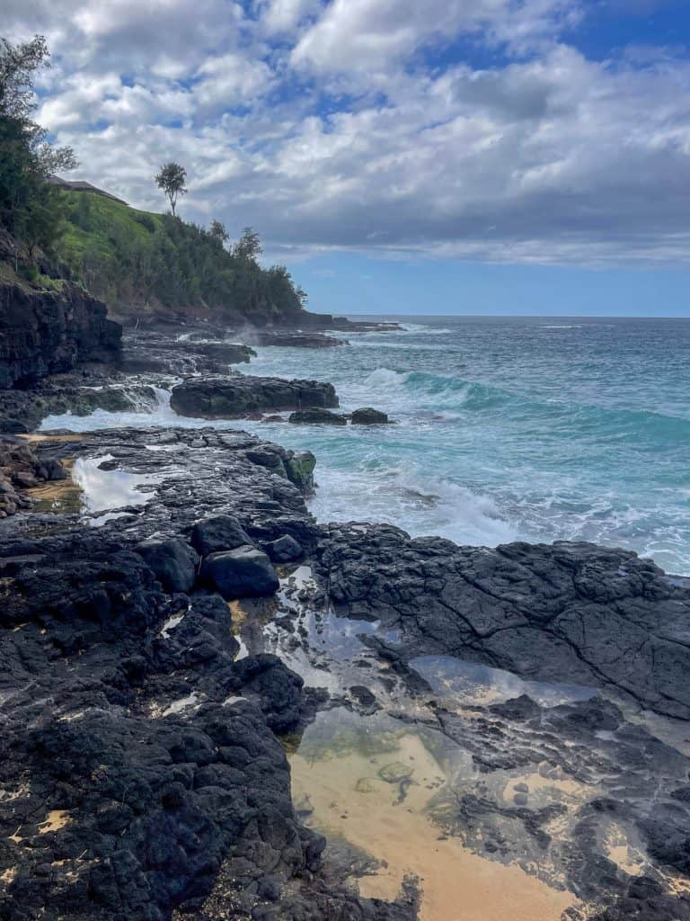 view of the vibrant blue ocean from the lava-rock and yellow sand covered beach