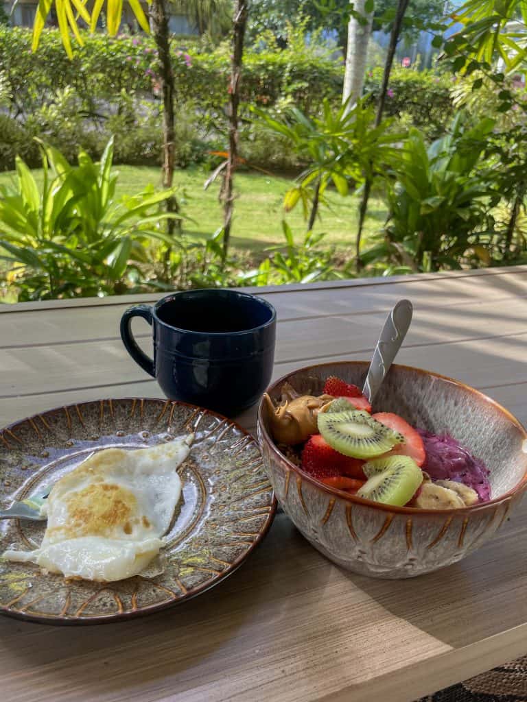 breakfast in a tropical lanai including a sunny side up egg, a coffee, and a smoothie bowl with strawberries, kiwi, and peanut butter