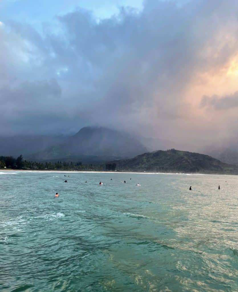 several surfers in the water at Hanalei Bay at sunset