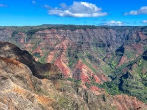 Waimea canyon overlook with vast red cliffs, greenery, and a large waterfall in the distance