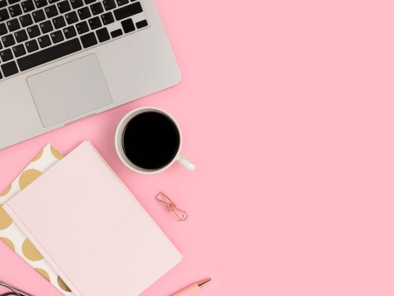 a macbook, notepad, and cup of coffee on a pink desk
