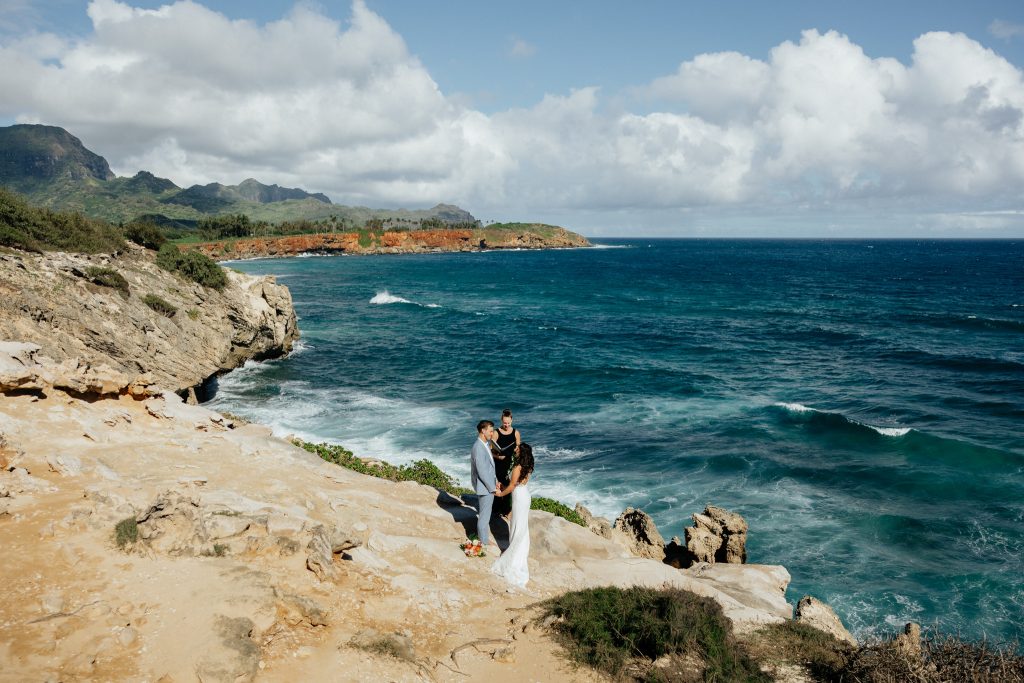 a couple getting married on Makawehi Bluffs in Kauai on sandy cliffs with the ocean and mountains in the distance