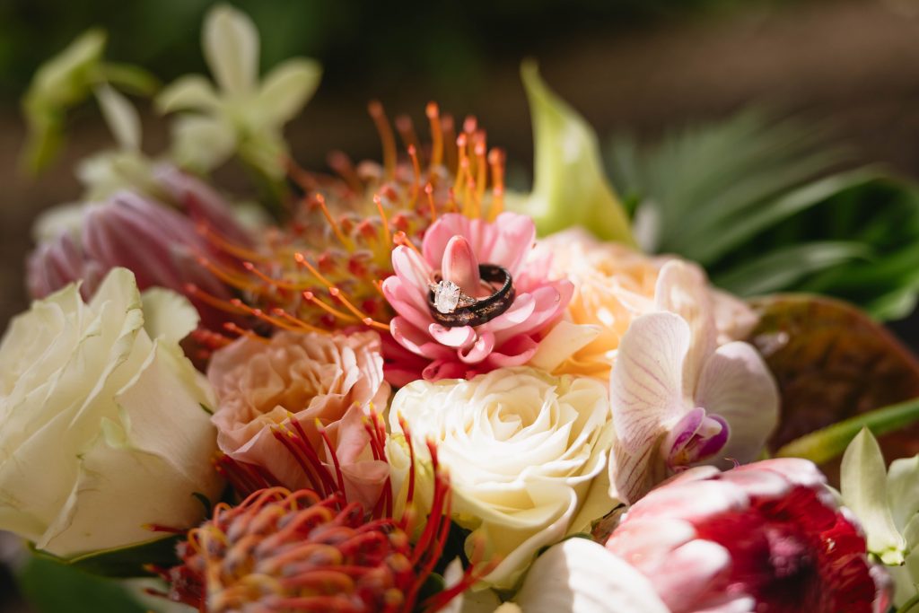 a wedding bouquet with white roses, orange lilies, and tropical pink flowers with wedding rings in the center