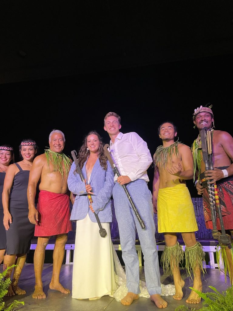 a newly wed couple standing on stage next to five Hawaiian Luau Fire Show preformers