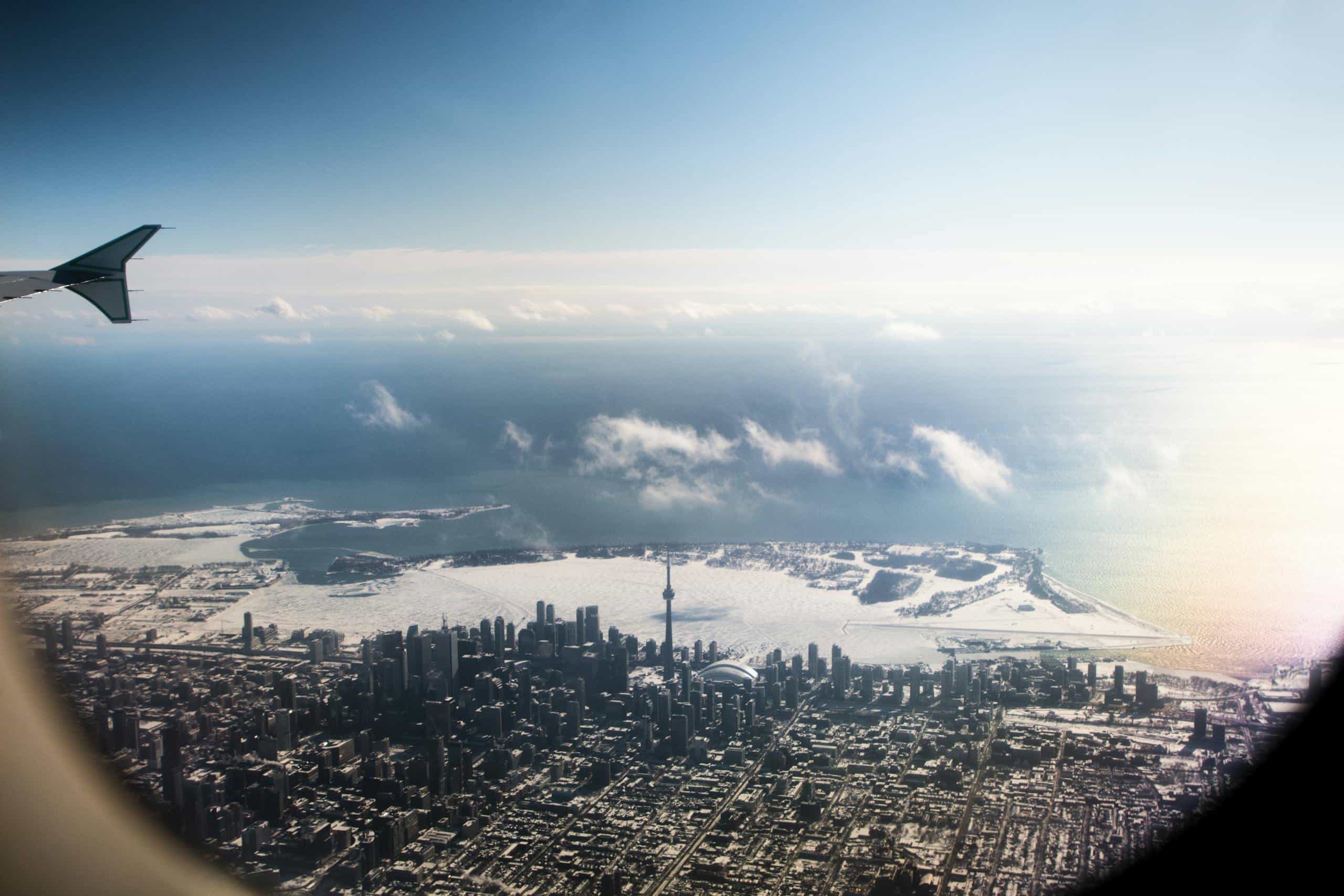 A stunning aerial view of Toronto skyline with the CN Tower and snowy landscape, seen from an airplane.
