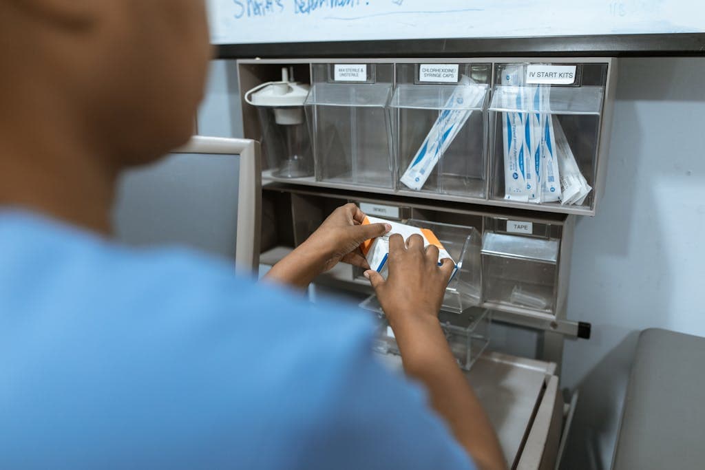 A travel nurse organizes medical supplies in a hospital setting. Focus on hands and storage unit with IV kits.