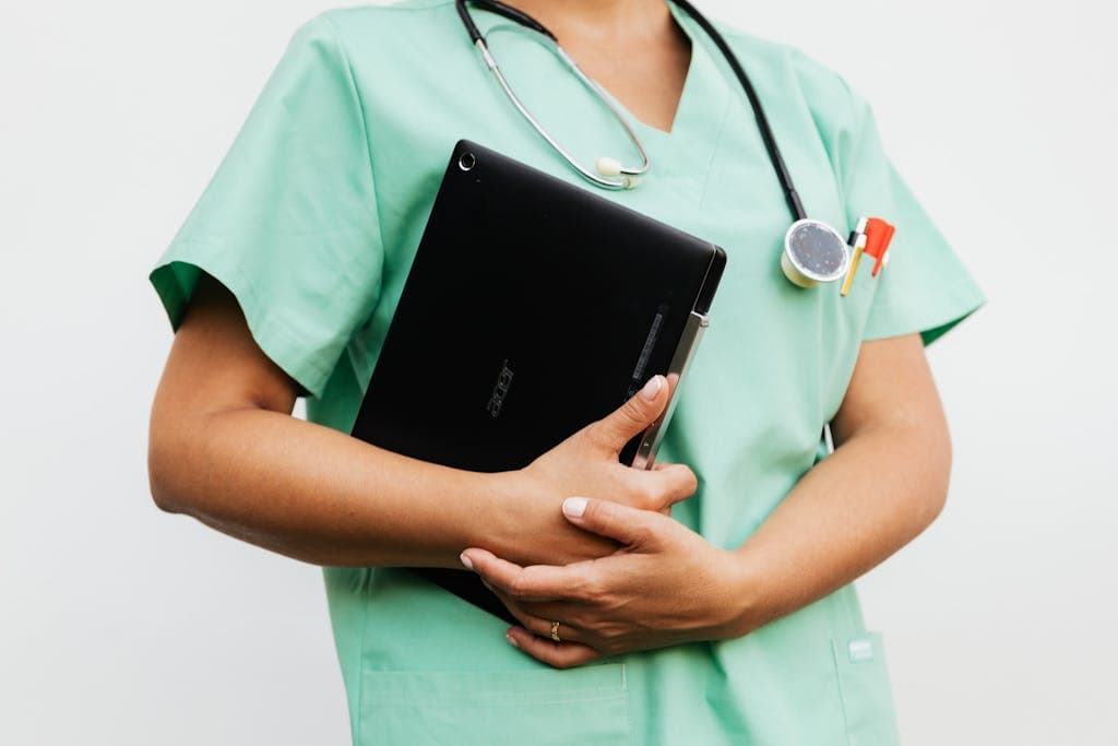 Close-up of a travel nurse in green scrubs holding a tablet and stethoscope