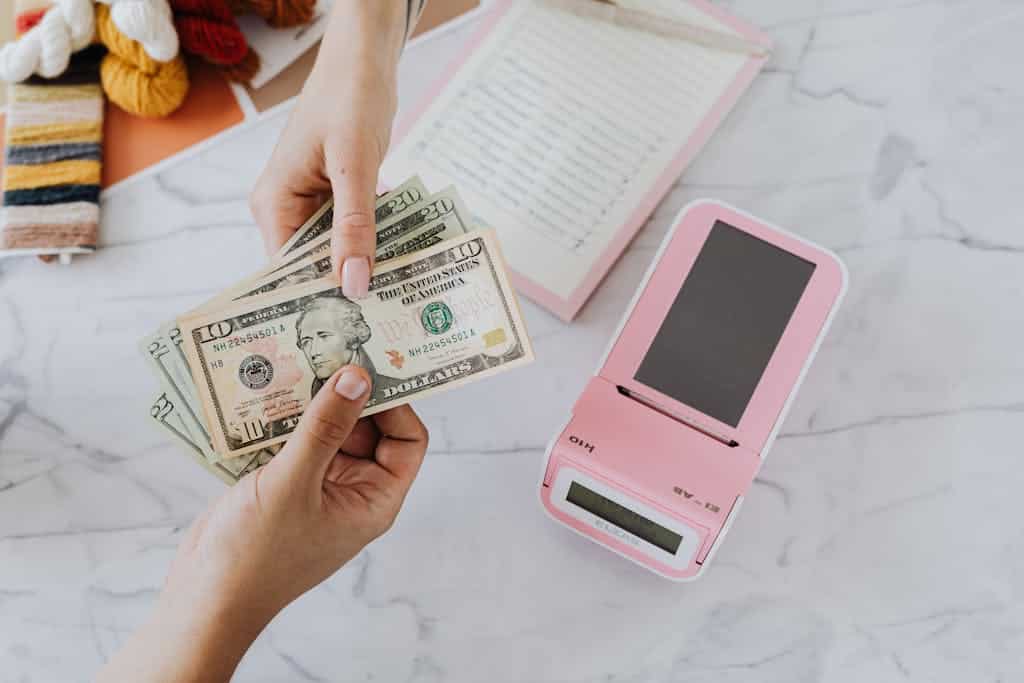 Close-up of hands exchanging US dollars with a pink calculator on a marble surface symbolizing negotiating travel nurse pay