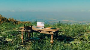 Image of a desk and computer in the grass on a scenic overlook eluding to a remote nurse job