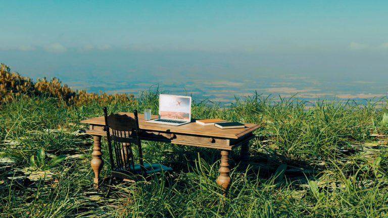 Image of a desk and computer in the grass on a scenic overlook eluding to a remote nurse job
